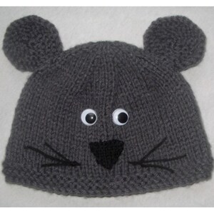 May include: A gray knitted hat with large, round ears, googly eyes, and a black nose and whiskers. The hat is designed to resemble a mouse. The hat is a cozy accessory for cold weather.