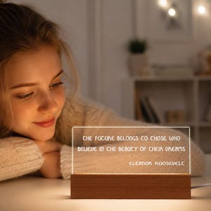 May include: A rectangular clear acrylic light panel set into a rectangular wooden base. The panel is illuminated and features the engraved text: The future belongs to those who believe in the beauty of their dreams. Eleanor Roosevelt.