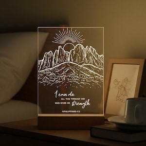 May include: A rectangular LED night light with a mountain and sun illustration and the text "I can do all things through Him who gives me strength". The light sits on a wooden base.