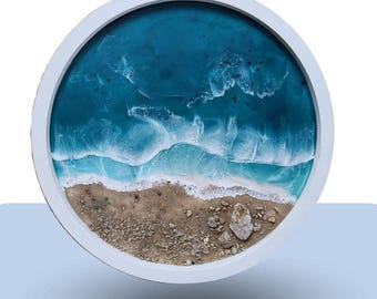 Könnte beinhalten: Ein rundes Harz-Kunstwerk, das eine Strandszene mit blauen Ozeanwellen darstellt, die an einem Sandufer brechen. Das Stück ist in einem weißen Kreis gerahmt.