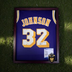 Puede incluir: Camiseta de baloncesto morada enmarcada con el nombre "JOHNSON" y el n&uacute;mero "32" en blanco y dorado. La camiseta se exhibe en un marco de madera oscura, con un certificado Beckett y un logotipo de Bullport.