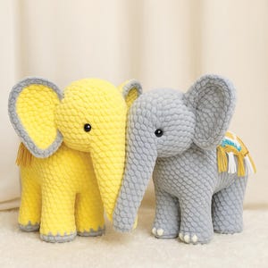 Op de afbeelding: Twee gehaakte knuffelelephantjes. Eentje is geel en de andere is grijs. Beide hebben een textuur en zwarte ogen.