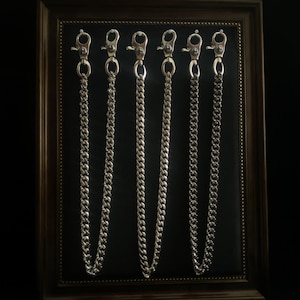 May include: Six silver-toned metal wallet chains arranged vertically, each featuring a polished curb link design and a swivel lobster clasp at the top. The chains are displayed against a dark background within a rectangular frame.