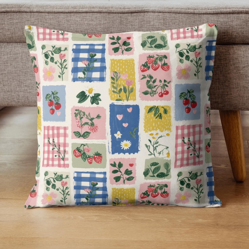 May include: Square throw pillow with a patchwork design featuring strawberries, flowers, and gingham patterns in pink, blue, yellow, and green. The pillow is a decorative home accent.