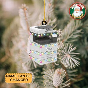 May include: A white and gray printer Christmas ornament with colorful string lights. The ornament has the word "Name" printed on it and a "Santa Approved" seal. The text "Name Can Be Changed" is on a yellow banner.