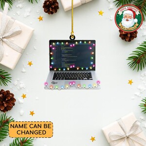 May include: A silver laptop Christmas ornament with a string of colorful lights around the screen and keyboard. The laptop screen displays code. The ornament has a gold string for hanging and the text "Name" is visible. The words "NAME CAN BE CHANGED" are also visible.