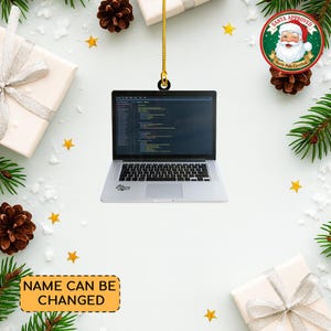 May include: A silver laptop ornament with a screen displaying code, hanging from a gold string. The ornament has a black keyboard and a small sticker. The background includes gifts, pine cones, stars, and a "Santa Approved" badge.