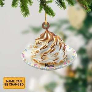May include: A Christmas ornament shaped like a baked dessert, featuring a white meringue top with toasted brown swirls, resting on a white plate with colorful lights. The word "Name" is printed on the plate.