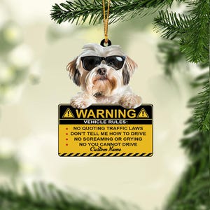 May include: A decorative ornament featuring a dog wearing sunglasses, holding a sign with the text "WARNING" and vehicle rules. The sign is yellow and black with a space for a custom name. The dog is white and brown.