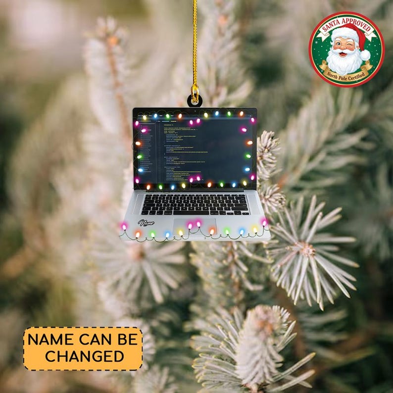 May include: A silver laptop Christmas ornament with a string of colorful lights around the screen and bottom. The laptop screen displays code. The ornament is hanging from a gold string. A Santa Approved sticker is in the background.