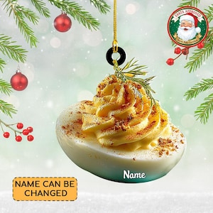 May include: Deviled egg Christmas ornament with a yellow filling, sprinkled with spices, and a sprig of rosemary. The ornament has a gold string and a black ring for hanging. The text "Name" is visible on the ornament. The text "Name Can Be Changed" is also visible.