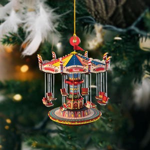 May include: A colorful carousel ornament with a gold string for hanging. The ornament features a red, yellow, and blue roof, with the word "Name" on the front. The carousel has red and yellow seats and a decorative base.