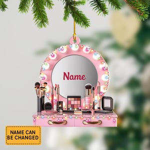May include: A pink vanity ornament with a mirror and makeup products. The mirror is surrounded by lights and has the word "Name" on it. The vanity has drawers and is decorated with lights. The text "NAME CAN BE CHANGED" is on a yellow rectangle.