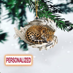 May include: A personalized Christmas ornament featuring a sleeping jaguar with a spotted coat, nestled on a bed of white feathers. The word "Name" is written in cursive. The word "PERSONALIZED" is in a red rectangle.