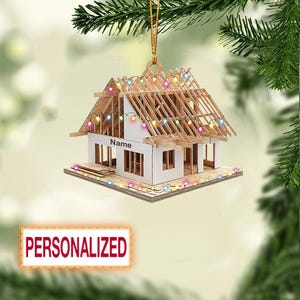 May include: A personalized wooden house ornament with a partially constructed roof, strung with colorful lights. The ornament has the word "Name" printed on the front and is suspended by a gold string. The word "PERSONALIZED" is printed on a red rectangle.