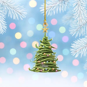 May include: A Christmas tree ornament shaped like a tree made of green beans, with a gold star on top and a string of colorful lights. The ornament has the word "Name" written on it. The background is a soft blue with bokeh lights.