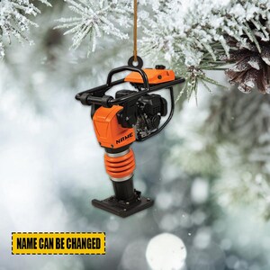 May include: An orange and black construction equipment ornament with the word "NAME" printed on the side. The ornament is hanging from a brown string. The text "NAME CAN BE CHANGED" is printed on a yellow rectangle.