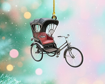 May include: A decorative ornament featuring a miniature rickshaw with a black canopy and red seat. The rickshaw has black wheels and a silver frame. The word "Name" is printed on the seat. The ornament is suspended by a gold string.