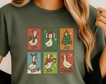 May include: Olive green t-shirt featuring a whimsical design of six postage stamp-style images. Each stamp showcases a goose in festive holiday attire, including a Santa hat, a gift, a Christmas tree, reindeer antlers, a scarf with a mug, and a musical note.
