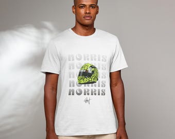 May include: White t-shirt with a repeated pattern of the word "MORRIS" in grey text. A yellow and black racing helmet is centred on the shirt. The helmet has a unique design with black and white markings. The signature "Lando Norris" is printed in grey below the helmet.