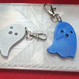 May include: Two ghost-shaped keychains, one blue and one white, with a silver key ring attached to each.