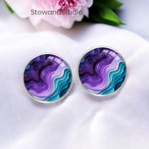 May include: A pair of round stud earrings with a silver-colored border. The earrings feature a layered design in shades of purple, teal, and white. The text "Stewanastudio" is visible in the background.