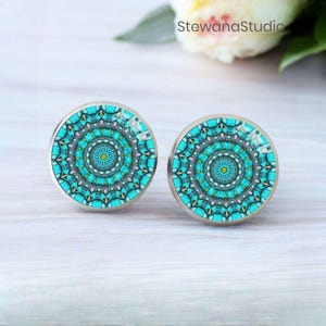 May include: Two round cabinet knobs with a mandala design in shades of turquoise, teal, and yellow. The knobs have a silver-colored metal base. The background includes a white surface and a flower. The text "StewanaStudio" is visible.