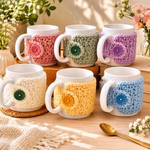 May include: Six white ceramic mugs, each wrapped in a removable, textured crochet cozy. The cozies come in pink, sage green, lavender, cream, yellow, and light blue, each secured with a matching round plastic button on the side of the handle.