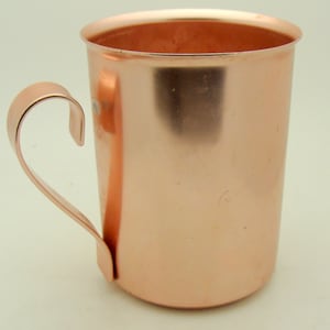May include: A copper mug with a handle. The mug is shiny and has a smooth surface.