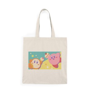 May include: Cream-colored tote bag featuring a colorful graphic of two cartoon characters. One is pink, the other is orange, and both are set against a background of yellow, teal, and stars. The bag has two cream-colored handles.