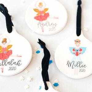 May include: Three white ceramic ornaments with a ballerina design. Each ornament features a different ballerina with a unique outfit and wings. The ornaments are personalized with the names "Audrey", "Tallulah", and "Millie" and the year "2020".