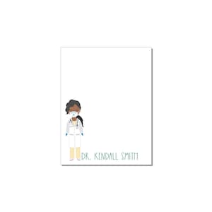 May include: A white notepad with a cartoon illustration of a Black doctor wearing a face mask, a white coat, and a stethoscope. The text "DR. KENDALL SMITH" is printed below the illustration.