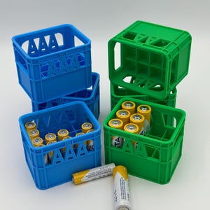 Könnte beinhalten: Eine Sammlung von blauen und grünen Kunststoff-Aufbewahrungsboxen für AAA-Batterien. Die Boxen haben eine gitterartige Struktur mit dem eingeprägten Text AAA an den Seiten. Mehrere gelbe und silberne AAA-Batterien befinden sich in den Boxen.