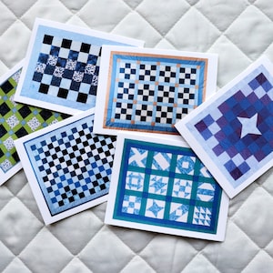 May include: Five different cards with blue and white checkered patterns. The cards are all different sizes and have different patterns. The cards are on a white quilted surface.