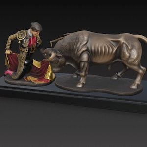 Puede incluir: Escultura de bronce que representa una escena de corrida. Un matador con traje tradicional está arrodillado, sosteniendo una capa roja, frente a un gran toro. La escultura está montada sobre una base rectangular negra.