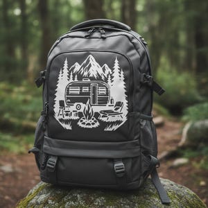 May include: A dark gray backpack with a white graphic of a camper, mountains, trees, and a campfire. The backpack has multiple compartments, straps, and mesh side pockets. Perfect for camping and outdoor adventures.