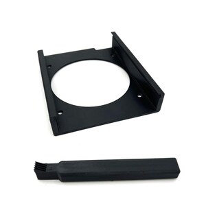Puede incluir: Soporte met&aacute;lico negro con una abertura circular y orificios de montaje, y un componente rectangular negro separado con un extremo en forma de cepillo. Los art&iacute;culos se muestran sobre un fondo blanco.