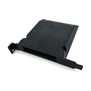 Op de afbeelding: Een zwart, rechthoekig 3D-geprint object met een sleuf en een uitstekende lip. Het object heeft een getextureerd oppervlak en lijkt een component of behuizing voor een elektronisch apparaat te zijn. Er zit een klein gaatje in.