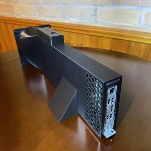Peut inclure: Un appareil &eacute;lectronique noir de forme rectangulaire avec une grille d'a&eacute;ration et plusieurs ports. Il est pos&eacute; sur une surface en bois et poss&egrave;de un support. Le design est inclin&eacute; vers le spectateur.