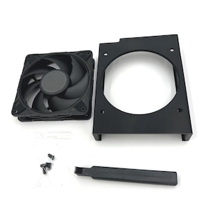 Puede incluir: Un ventilador de ordenador negro con siete aspas, un soporte de montaje negro, un cepillo peque&ntilde;o y tornillos. El ventilador tiene un cubo central y est&aacute; dise&ntilde;ado para enfriar componentes de ordenador. Los componentes est&aacute;n dispuestos sobre una superficie blanca.