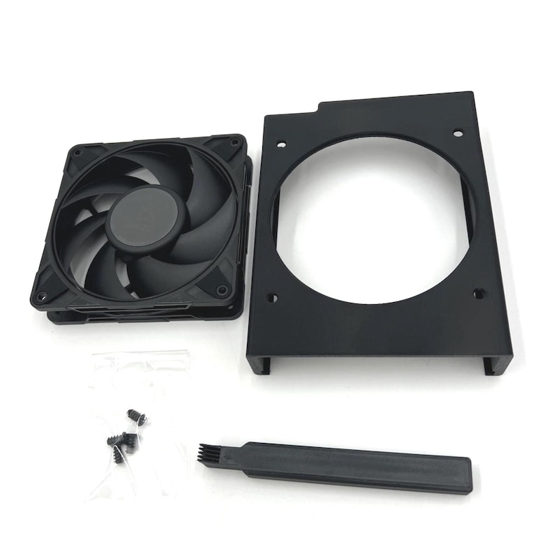 Puede incluir: Un ventilador de ordenador negro con siete aspas, un soporte de montaje negro, un cepillo peque&ntilde;o y tornillos. El ventilador tiene un cubo central y est&aacute; dise&ntilde;ado para enfriar componentes de ordenador. Los componentes est&aacute;n dispuestos sobre una superficie blanca.