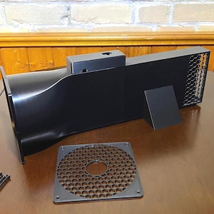 Peut inclure: Un syst&egrave;me d'admission d'air noir rectangulaire avec une grille en nid d'abeille, une plaque carr&eacute;e s&eacute;par&eacute;e et un petit support. Le syst&egrave;me a une entr&eacute;e incurv&eacute;e et une sortie rectangulaire avec une grille m&eacute;tallique. Plusieurs vis sont &eacute;galement pr&eacute;sentes.