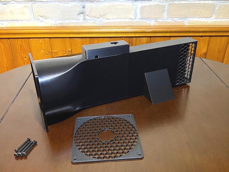 Peut inclure: Un syst&egrave;me d'admission d'air noir rectangulaire avec une grille en nid d'abeille, une plaque carr&eacute;e s&eacute;par&eacute;e et un petit support. Le syst&egrave;me a une entr&eacute;e incurv&eacute;e et une sortie rectangulaire avec une grille m&eacute;tallique. Plusieurs vis sont &eacute;galement pr&eacute;sentes.
