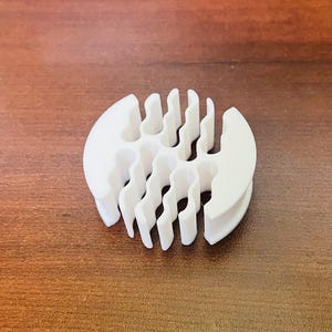 May include: White plastic cable organizer with multiple slots for cords and wires. The organizer is shaped like a circle with a flat base.