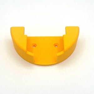 May include: A vibrant yellow, semi-circular wall mount with two small holes and two rectangular extensions. The mount is made of a solid, smooth material, designed to hold an item.