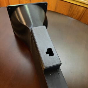Peut inclure: Un objet noir imprim&eacute; en 3D avec un dessus carr&eacute; et un corps &eacute;vas&eacute; et incurv&eacute;. Il poss&egrave;de une extension rectangulaire avec une d&eacute;coupe carr&eacute;e. L'objet est probablement un composant ou une partie d'une structure plus grande.