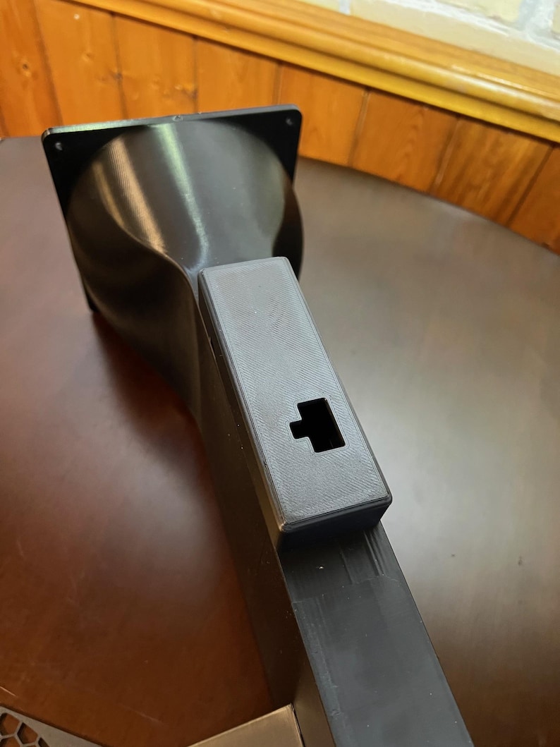 Peut inclure: Un objet noir imprim&eacute; en 3D avec un dessus carr&eacute; et un corps &eacute;vas&eacute; et incurv&eacute;. Il poss&egrave;de une extension rectangulaire avec une d&eacute;coupe carr&eacute;e. L'objet est probablement un composant ou une partie d'une structure plus grande.