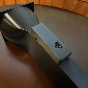 Peut inclure: Un appareil noir angulaire avec une base rectangulaire et un dessus incurv&eacute; en forme d'entonnoir. Un petit composant rectangulaire avec une s&eacute;rie de petites ouvertures est fix&eacute; sur le c&ocirc;t&eacute;. L'appareil semble &ecirc;tre fait d'un mat&eacute;riau mat.