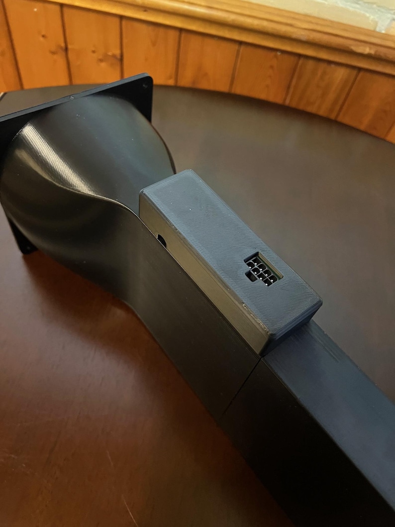 Peut inclure: Un appareil noir angulaire avec une base rectangulaire et un dessus incurv&eacute; en forme d'entonnoir. Un petit composant rectangulaire avec une s&eacute;rie de petites ouvertures est fix&eacute; sur le c&ocirc;t&eacute;. L'appareil semble &ecirc;tre fait d'un mat&eacute;riau mat.