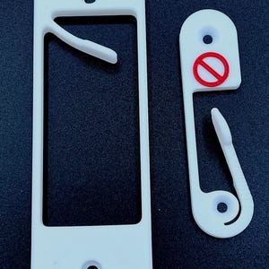 Könnte beinhalten: Weiße Wandhalterung aus Kunststoff mit einem Haken und einem Schlitz für ein Telefon oder ein anderes Gerät. Der Haken hat einen roten Kreis mit einem diagonalen Strich durch.